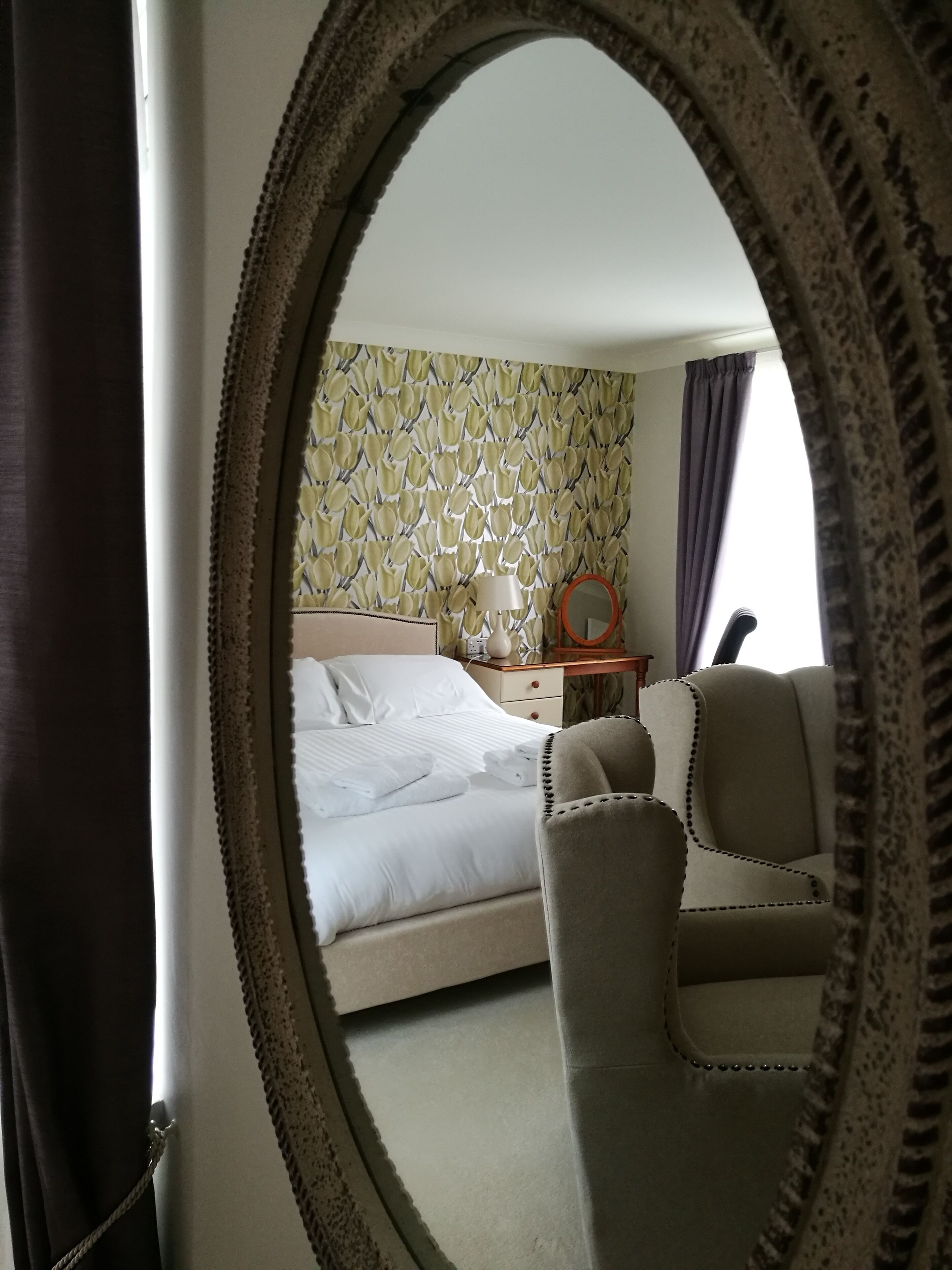 A bedroom with a bed, a chair, a nightstand, and a mirror.
