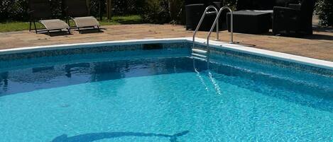 A clear blue pool with a ladder, surrounded by outdoor furniture and greenery.
