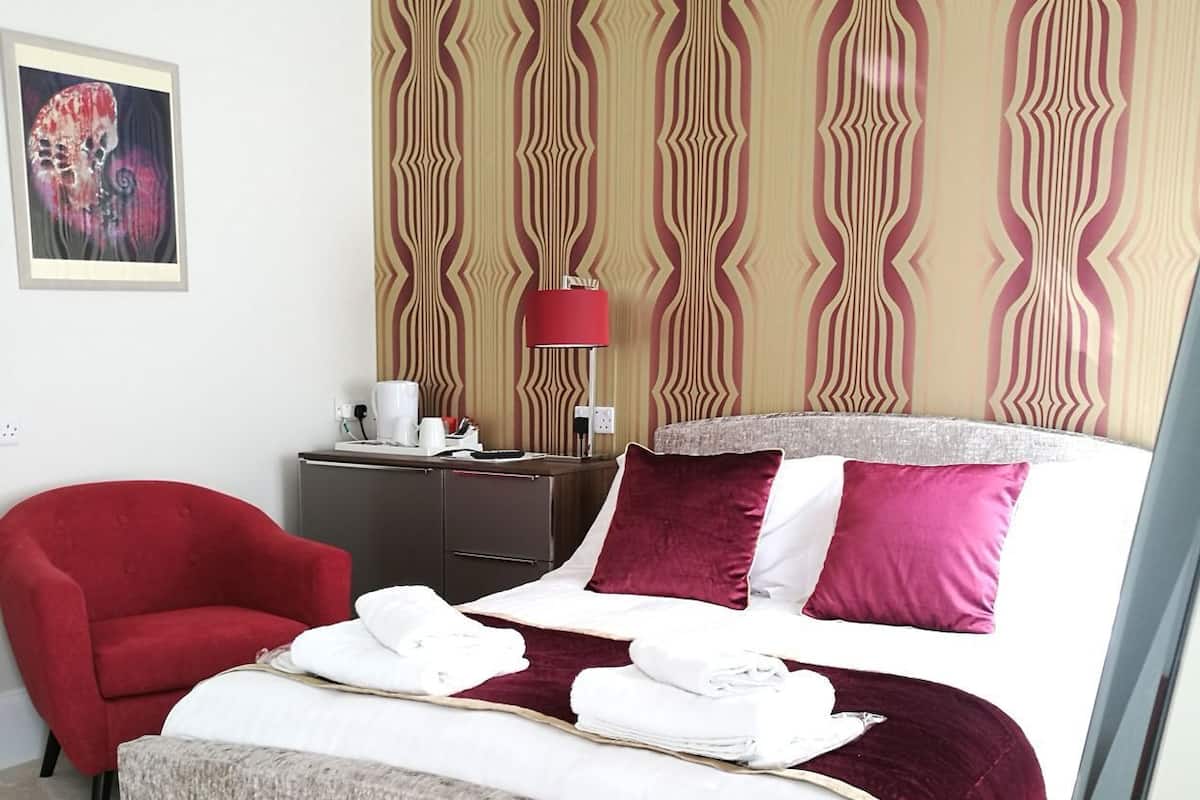 A hotel room with a bed, a red chair, a nightstand, a lamp, and a wall with a striped pattern.
