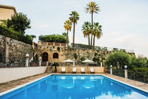Una piscina con un muro de piedra y palmeras al fondo.