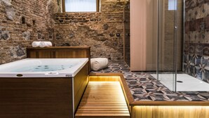 A stone-walled bathroom with a wooden bench, a bathtub, and a shower area. - Villa Pulejo (Messina)