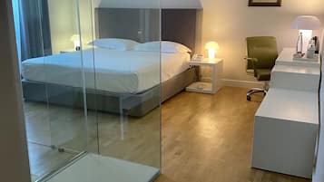 Habitación de hotel con cama, mesita de noche con lámpara, una silla y un escritorio con lámpara.