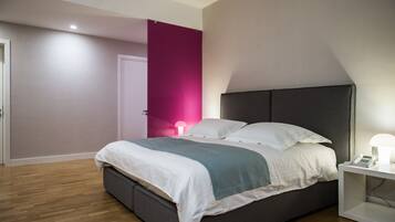 A modern bedroom with a bed, bedside table, and a nightstand with a lamp.