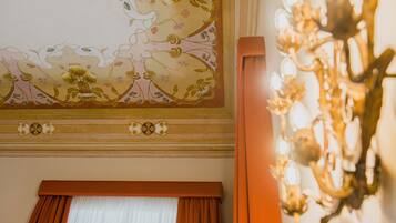 Une pièce dont le plafond est décoré de motifs floraux, avec une grande fenêtre agrémentée de rideaux et un lustre.