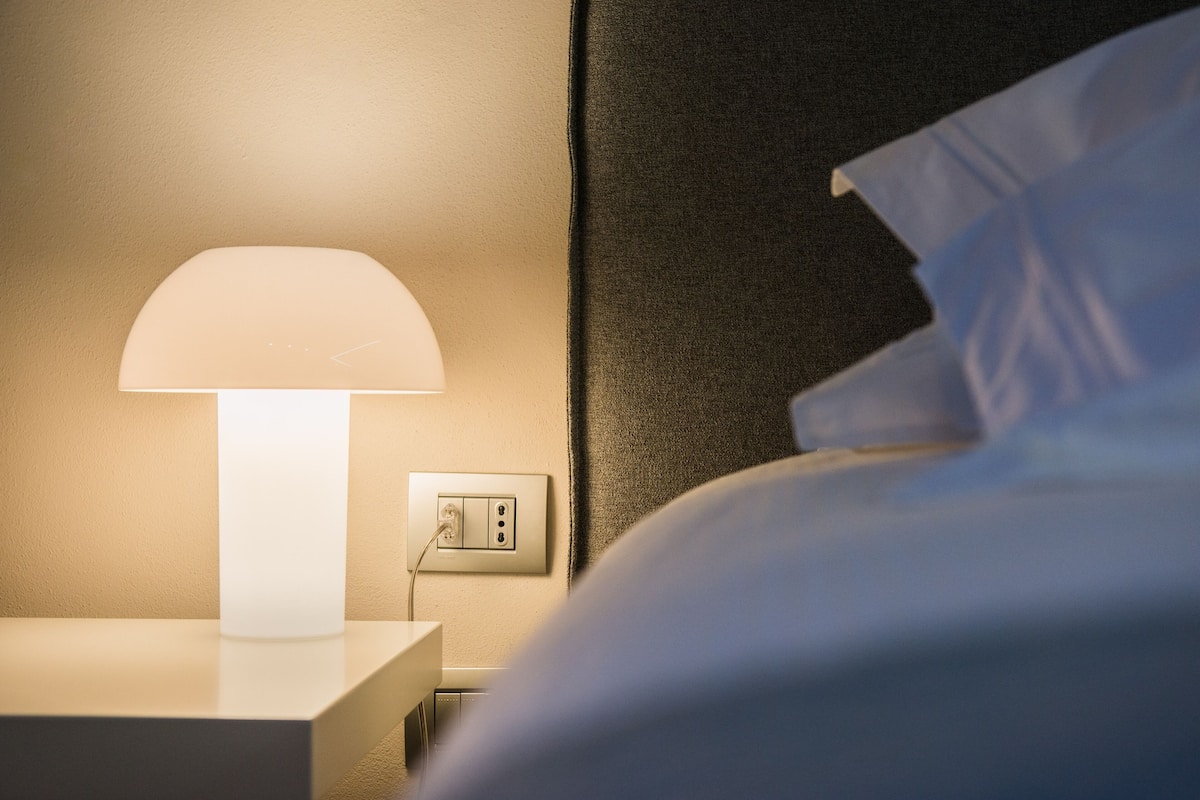 Eine Nachttischlampe, eine Steckdose und ein Bett mit weißer Bettwäsche.