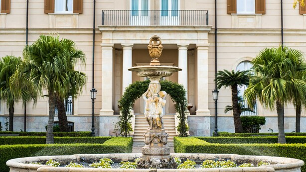 A fountain with a statue in front of a building with columns and windows. - Villa Pulejo (Messina)