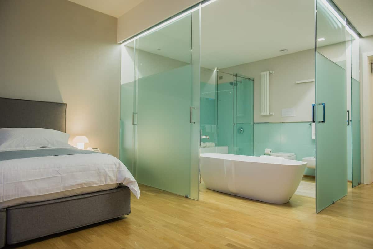 Ein modernes Schlafzimmer mit einem großen Bett, einer gläsernen Dusche und einem separaten Badezimmer mit einer Badewanne.