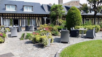 Sit and dine in the charming outdoor seating area, surrounded by lush greenery and the building's traditional half-timbered facade.