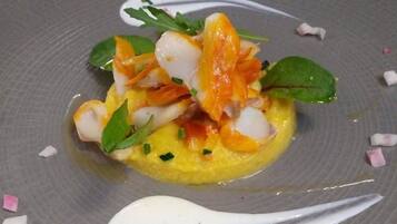 A plated dish with a yellow base, white and orange elements, green leaves, and white sauce.