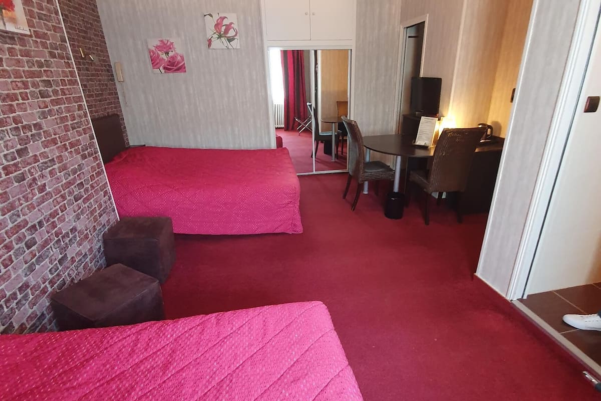 Habitación de hotel con dos camas, una mesita con una silla, televisión y espejo.