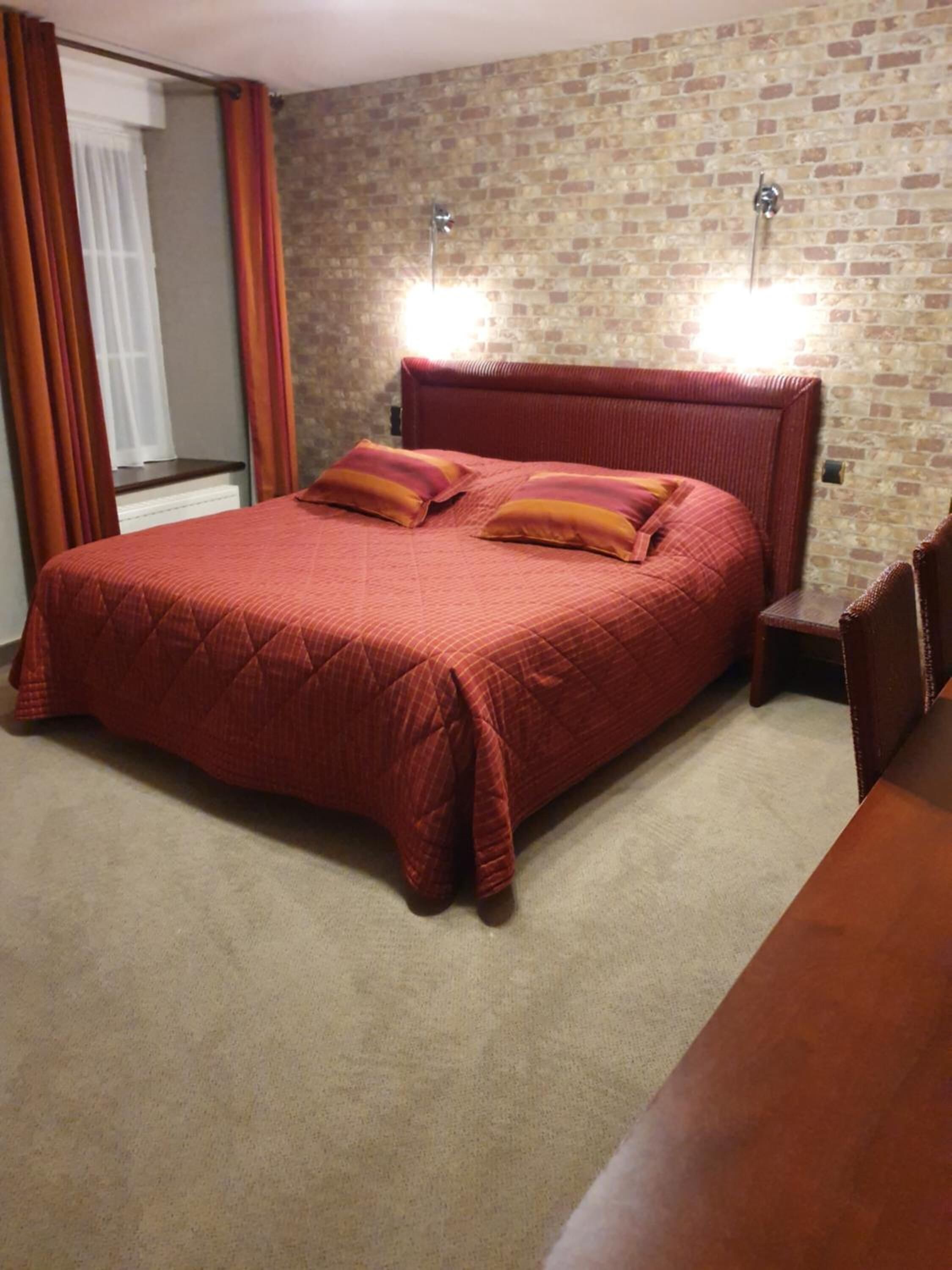 Camera da letto con parete in mattoni, un letto grande con testiera rossa, due abat-jour e un comodino in legno.