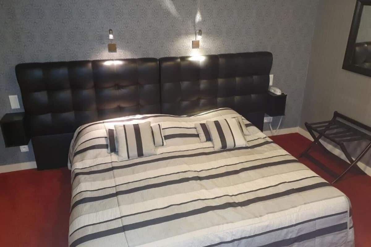 Habitación de hotel con una cama grande, ropa de cama a rayas, un cabecero capitonado, lámparas de noche y una alfombra roja.