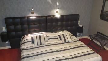Una camera d'albergo con un letto grande, biancheria a righe, un poggiatesta trapuntato, lampade ai comodini e un tappeto rosso.