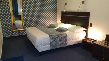 Una habitación de hotel con papel tapiz estampado, una cama con ropa de cama blanca y almohadas estampadas, una mesita de noche con una lámpara y un espejo en la pared.