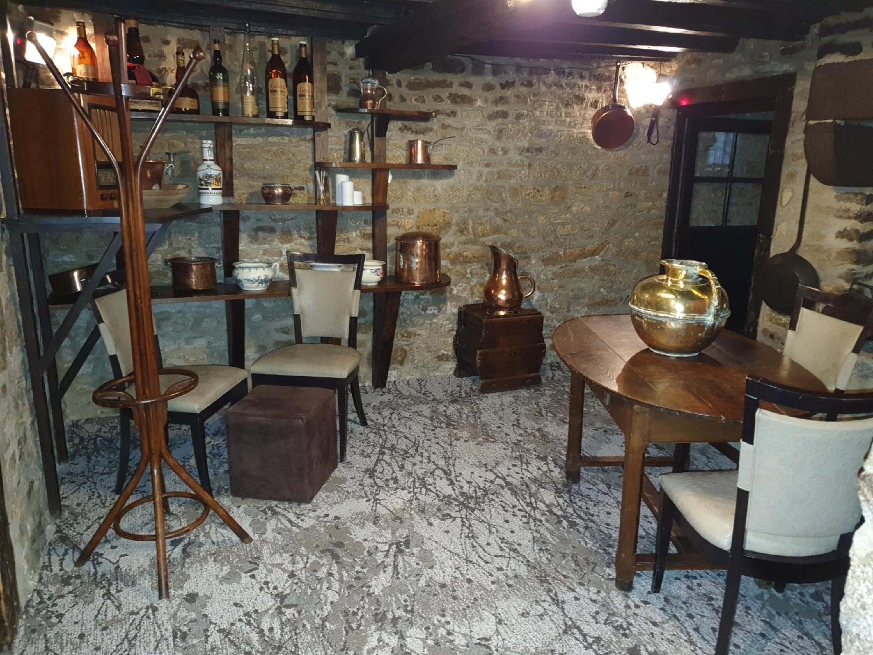A rustic room with exposed brick walls, wooden furniture, and shelves filled with bottles and copper pots.