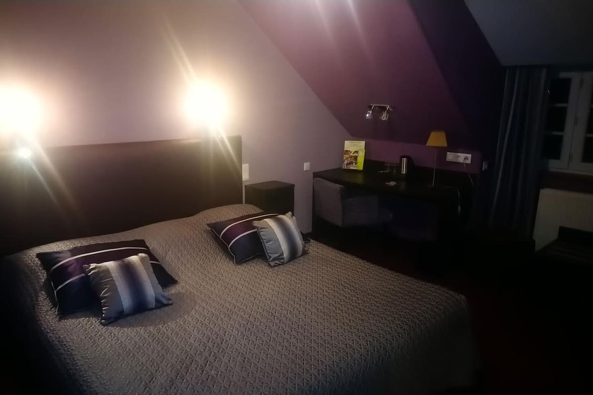Habitación de hotel con cama, dos lámparas de noche, un escritorio con silla y una ventana con cortinas.
