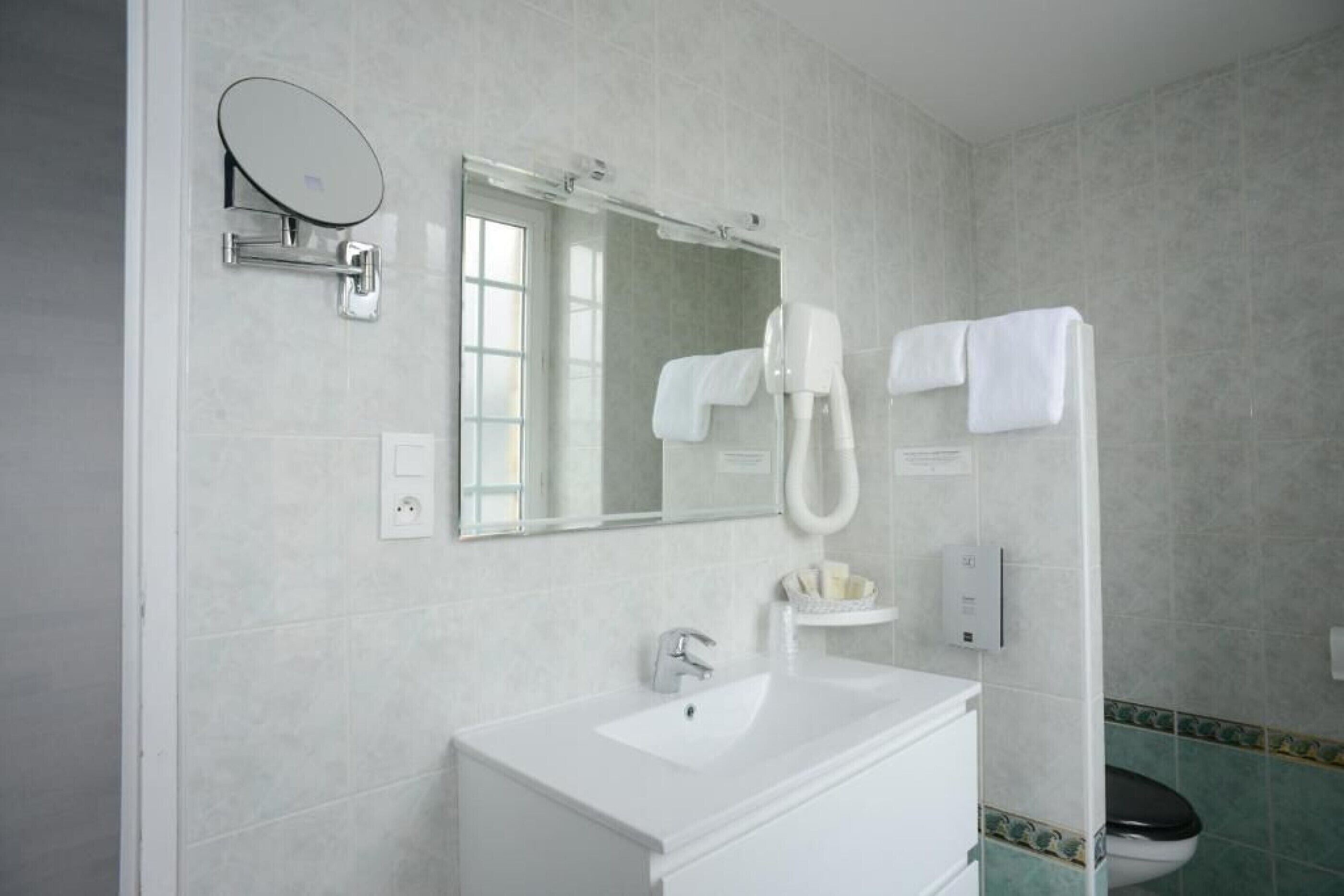 Un baño con lavamanos blanco, un espejo, cabezal de ducha de mano y un inodoro.