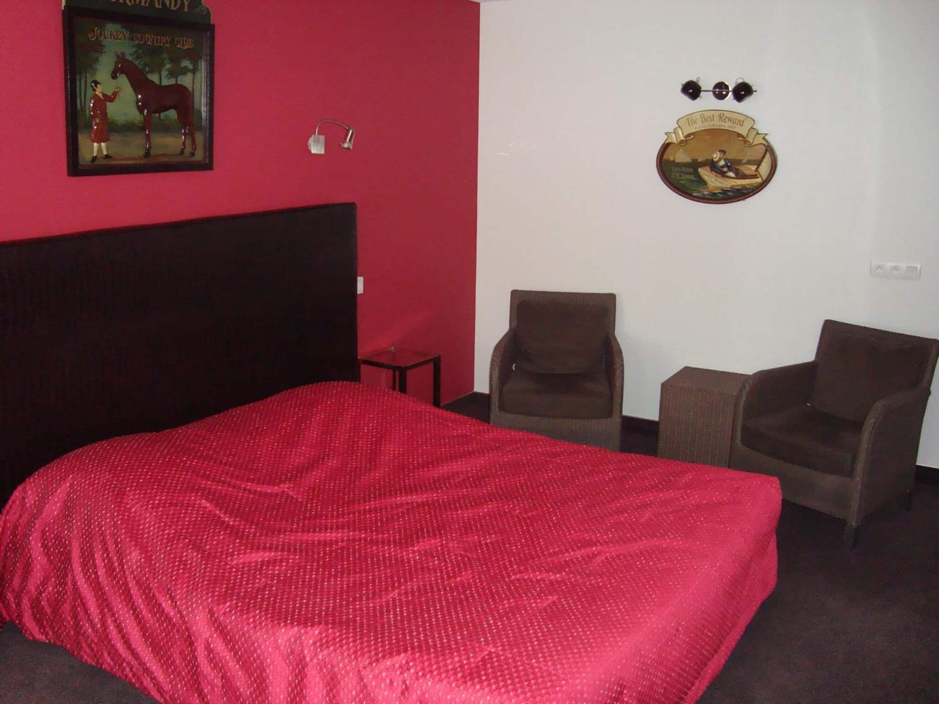 A hotel room with a large bed, two armchairs, a small table, and a wall with a horse painting and a plaque.