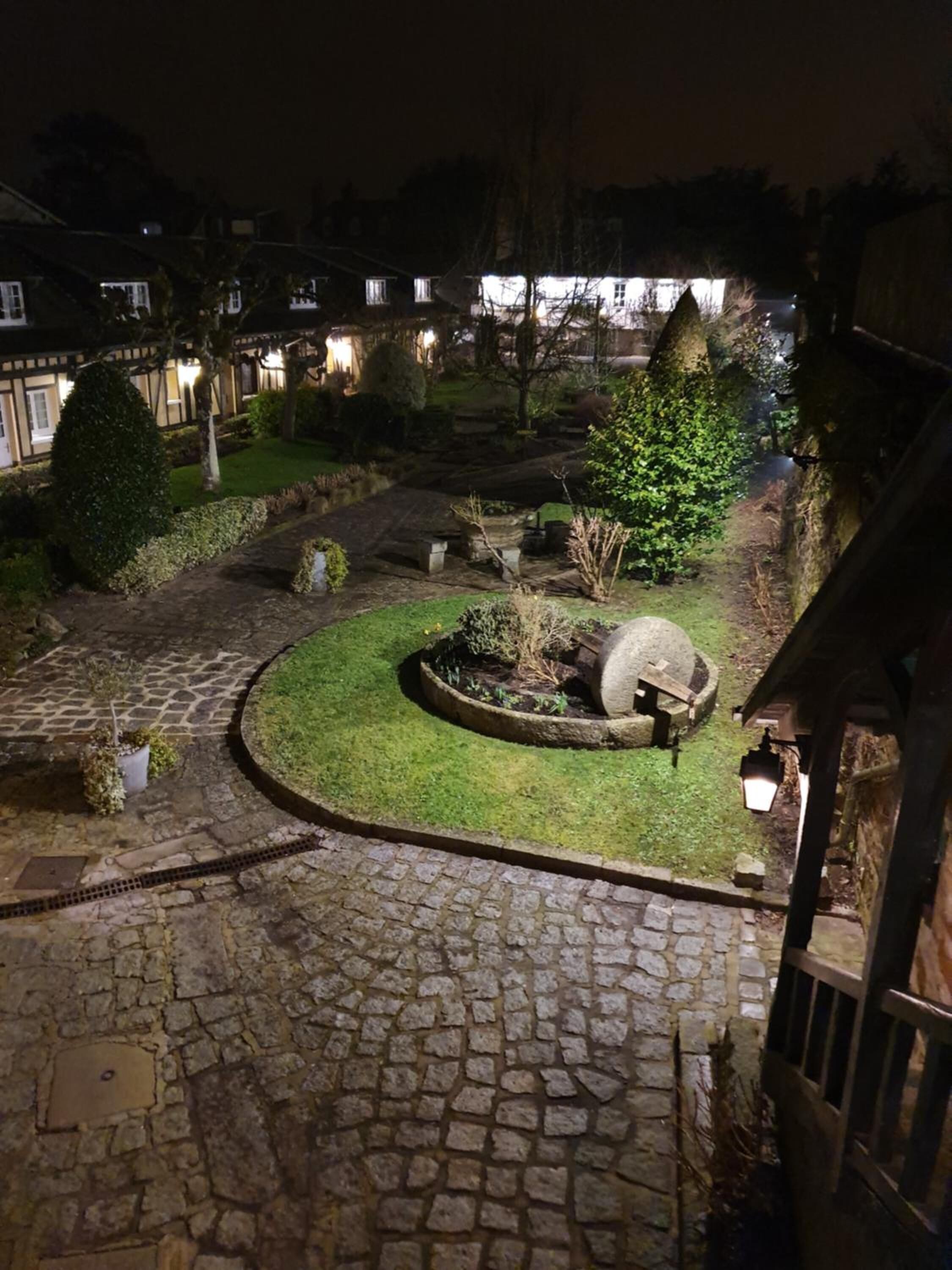 Un patio de piedra con un jardín circular, una gran fuente de agua y un sendero de piedra.