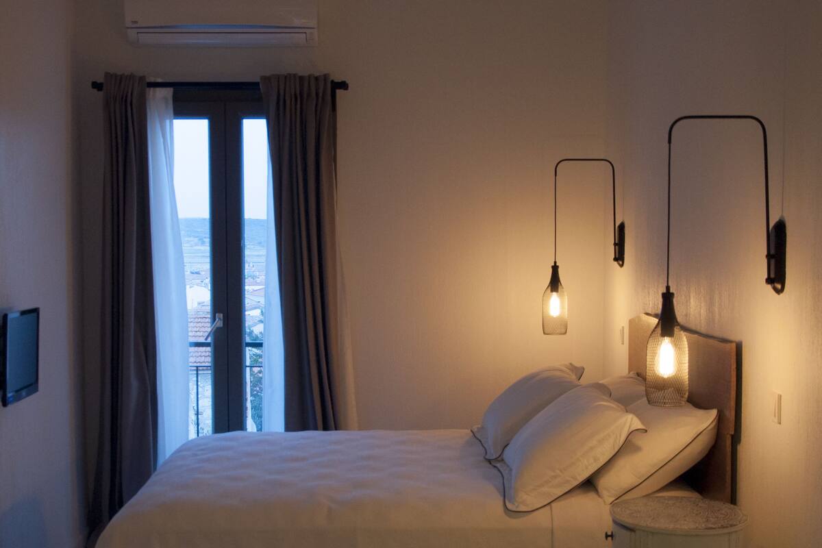 A bedroom with a bed, bedside table, and a view through a window.