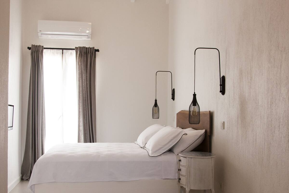 A bedroom with a bed, bedside table, lamp, and a chair.