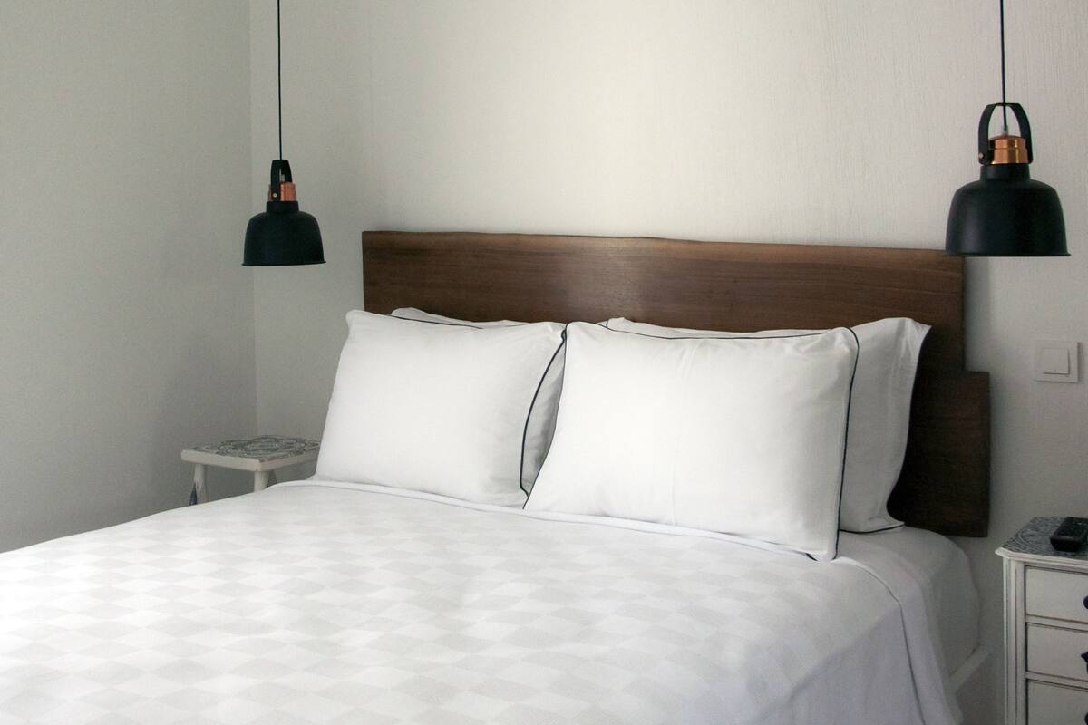 A neatly made bed with white linens, a wooden headboard, and two bedside lamps.