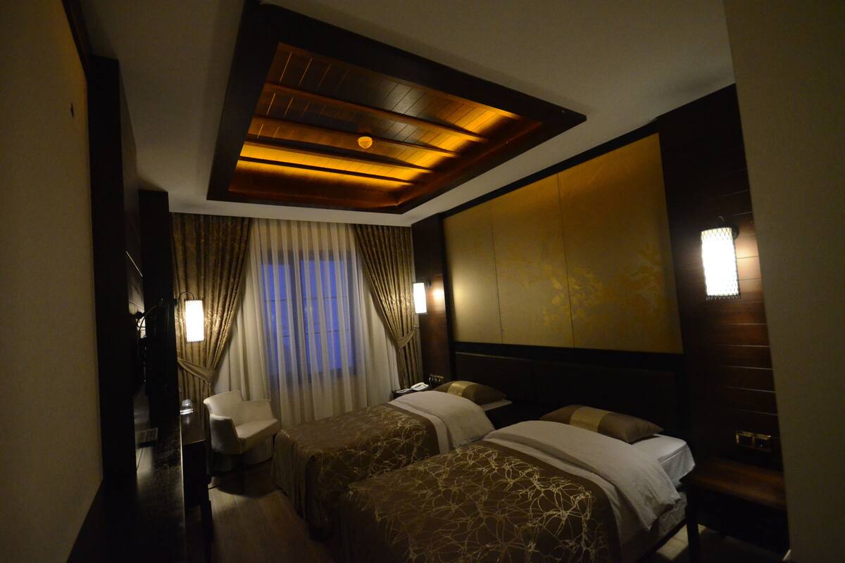 Habitación de hotel con dos camas, un escritorio y un ventanal grande con cortinas.
