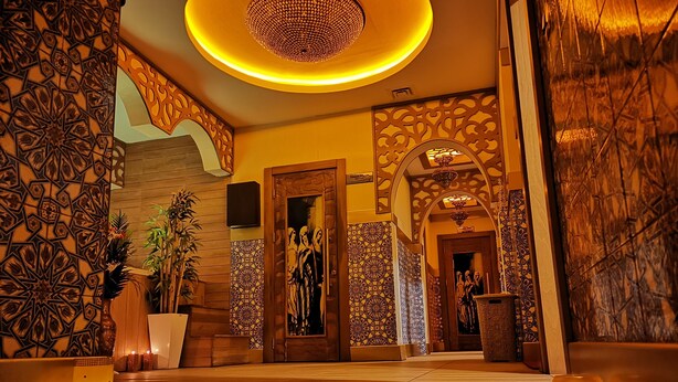 Un hall d’entrée doté d’un plancher en bois, de motifs décoratifs sur les murs, d’un grand lustre et d’un comptoir de réception.