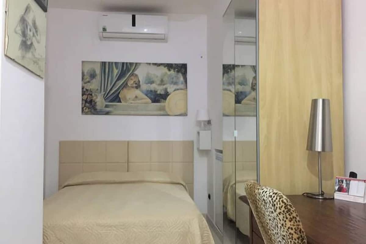 A hotel room with a bed, a painting on the wall, a mirror, a leopard print chair, and a desk with a lamp.