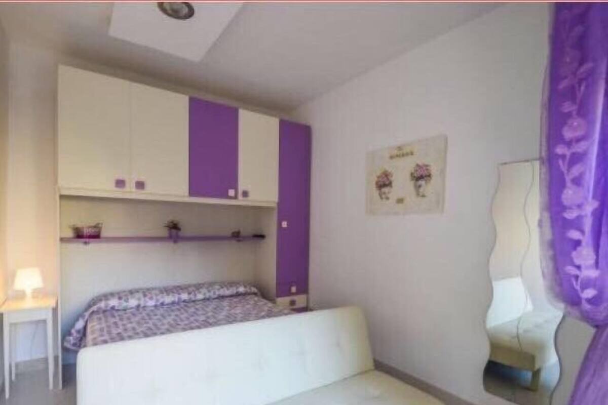 A bedroom with a bed, a small table, a mirror, and a wall-mounted cabinet.
