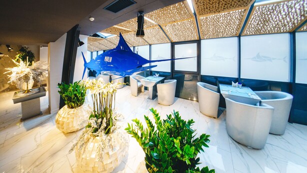 A modern interior with a blue sculpture, seating areas, and potted plants. - Marlin Hotel (Odesa)