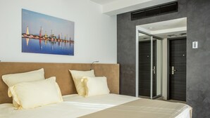 A modern hotel room with a large bed, a painting of a cityscape, and a door leading to a bathroom. - Marlin Hotel (Odesa)