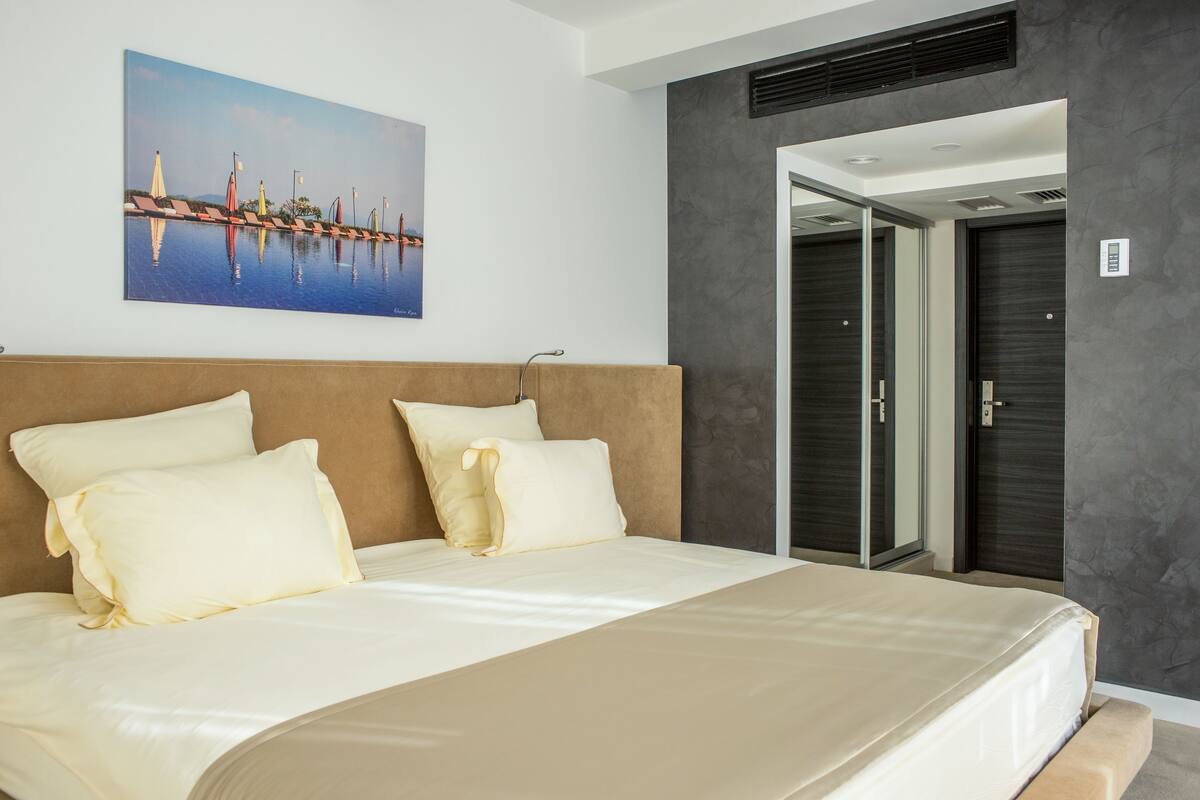 A modern hotel room with a large bed, a painting of a cityscape, and a door leading to a bathroom.