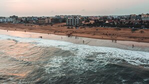 Une plage avec des vagues, des gens et des bâtiments en arrière-plan.