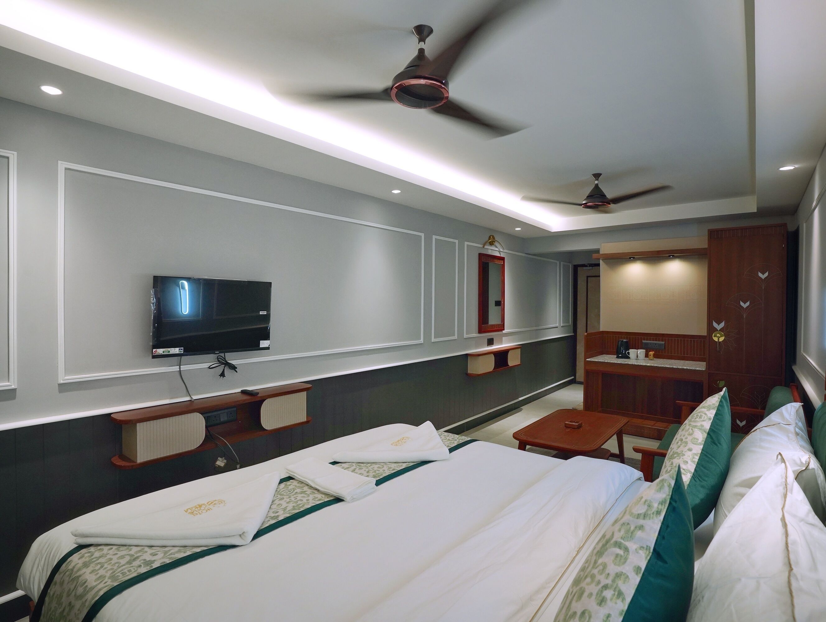 A hotel room with a bed, a TV, a mirror, a desk, and a ceiling fan.