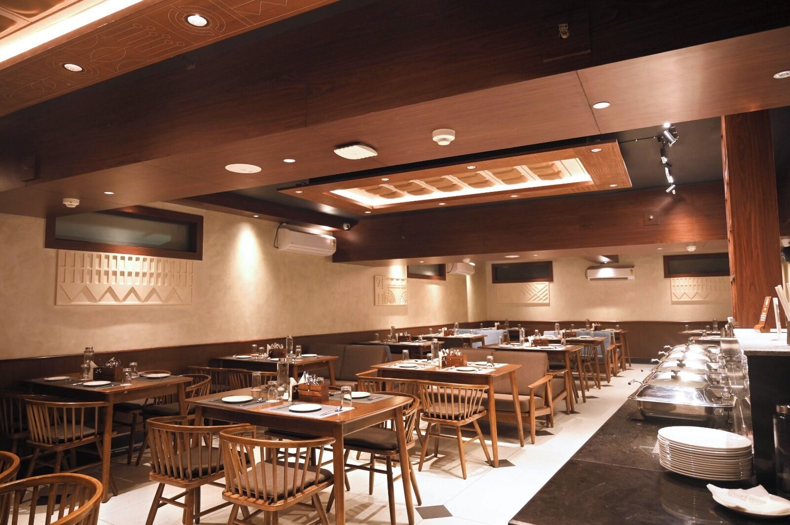 Een restaurant met meerdere tafels en stoelen, houten vloeren en inbouwverlichting.