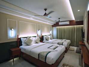 Habitación de hotel con dos camas, ventilador de techo, aire acondicionado y televisor.