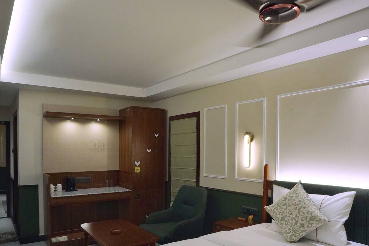 Ett hotellrum med en säng, ett skrivbord, en stol, en garderob och en takfläkt.