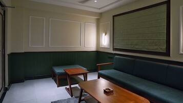 A room with a green upholstered sofa, a wooden coffee table, a small wooden table, and a bench.