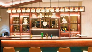 Un espace bar doté d’un comptoir en bois, de plusieurs étagères où sont rangés des verres, et de luminaires suspendus.