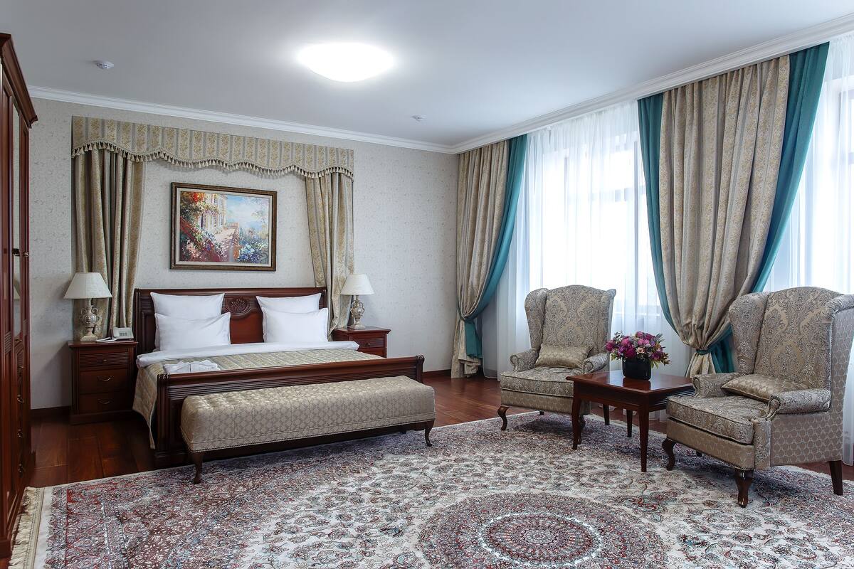 Ein Hotelzimmer mit einem großen Bett, zwei Sesseln, einem kleinen Tisch und einem dekorativen Teppich.