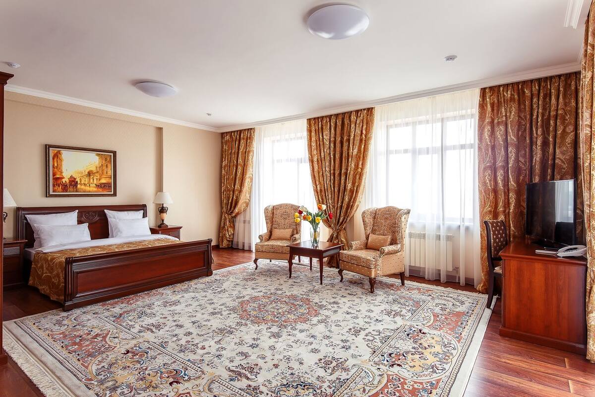 Ein Hotelzimmer mit einem großen Bett, zwei Sesseln, einem Couchtisch, einem Fernseher und einem Bild an der Wand.