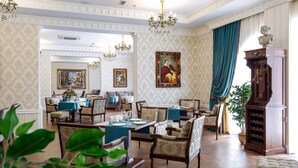 A formal dining room with wooden furniture, chandeliers, and a large painting on the wall. - Alanda Hotel (Astana)