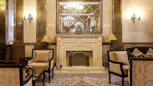 A grand lobby with a marble fireplace, ornate wall sconces, and classic furniture. - Alanda Hotel (Astana)