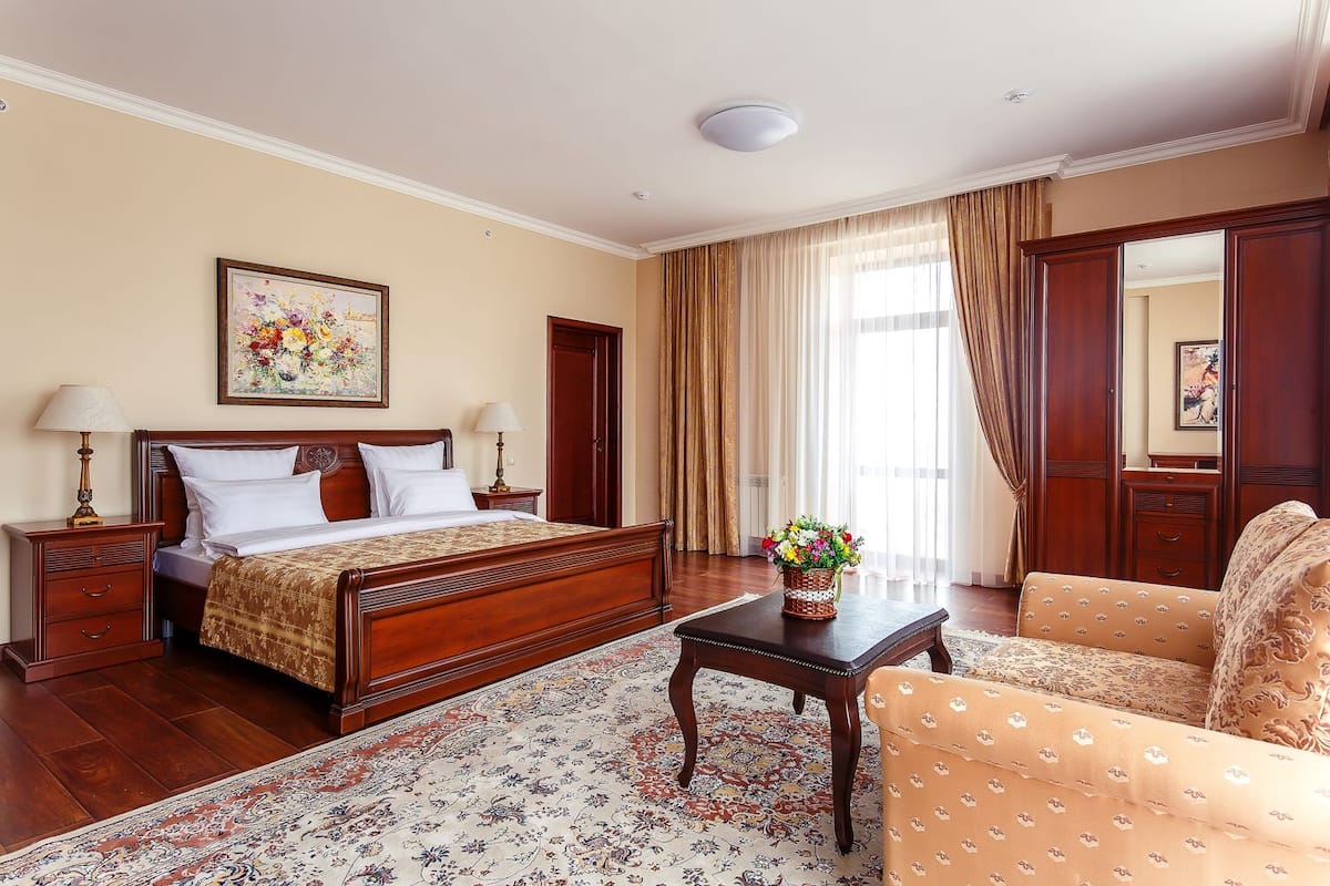 Ein Hotelzimmer mit einem großen Bett, zwei Nachttischen, einem Beistelltisch, einem Holzstuhl, einem kleinen Tisch mit Blumen und einem großen Spiegel.
