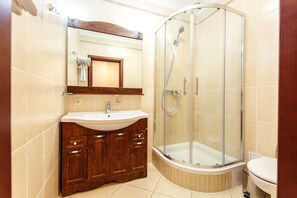 A modern bathroom with a curved shower enclosure, a wooden vanity with a sink, and a large mirror above the vanity. - Alanda Hotel (Astana)