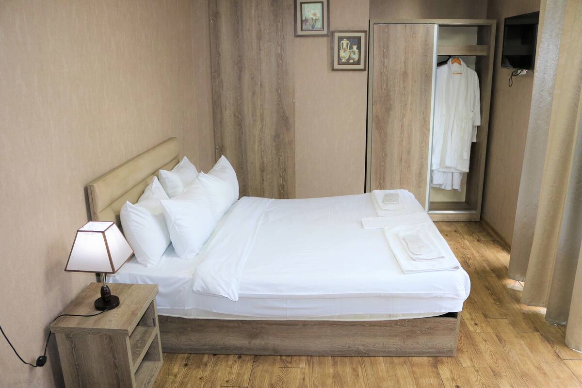 A neatly made bed with white linens, a bedside lamp, and a wooden nightstand.
