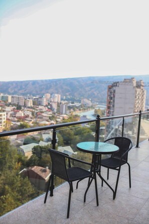 A balcony with a table and chairs, overlooking a cityscape with buildings and a river.