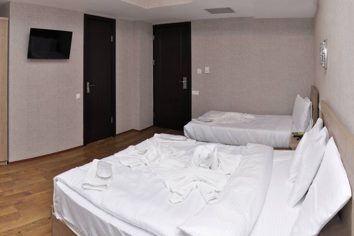 A hotel room with two beds, a wardrobe, a flat-screen TV, and a wooden floor.