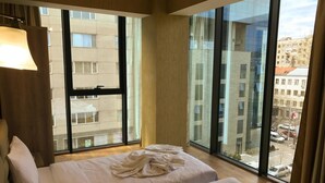 A hotel room with two beds, large windows, and a view of the cityscape. - L Plaza Hotel (Tbilisi)